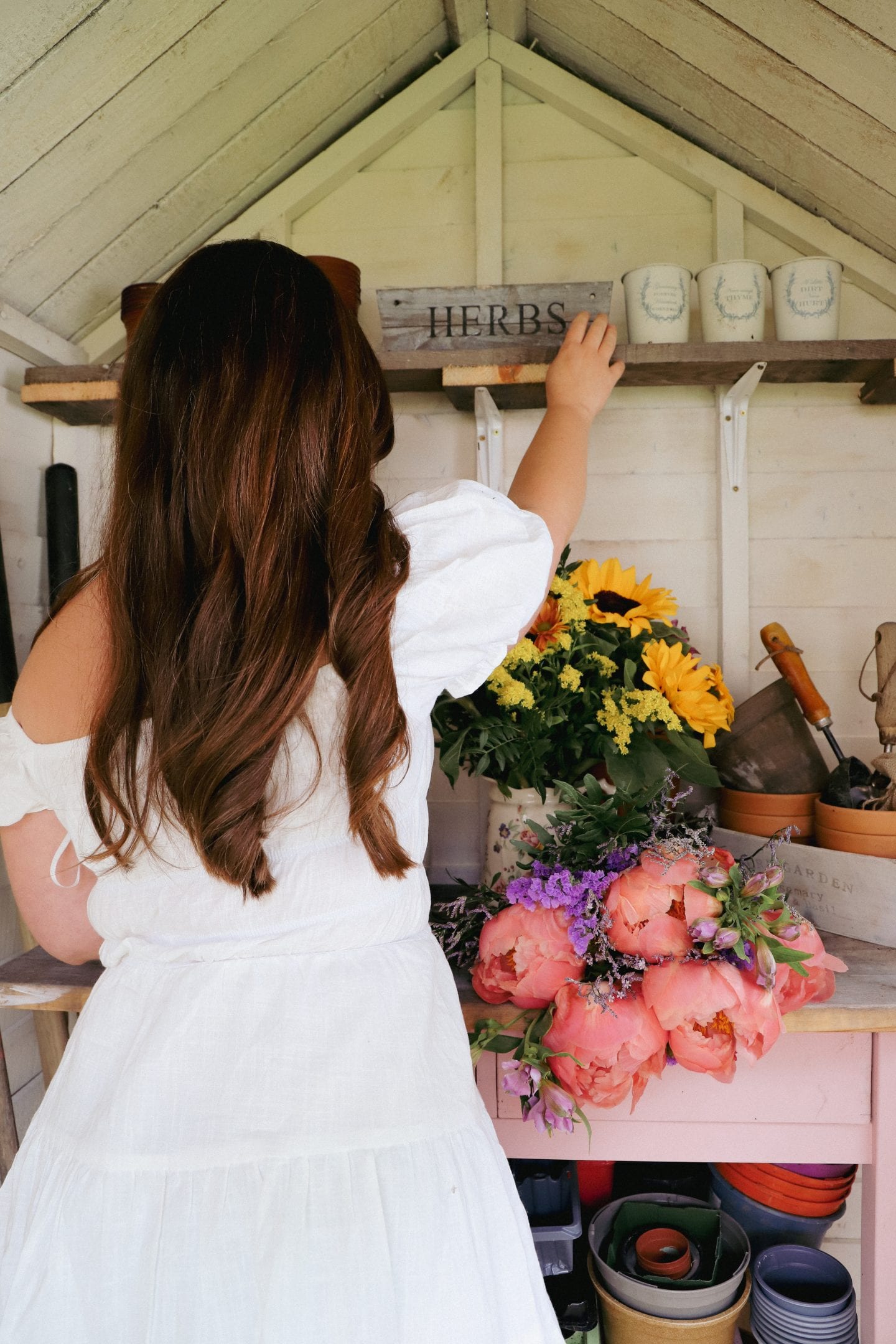 Girl in white dress in she shed, with flowers.